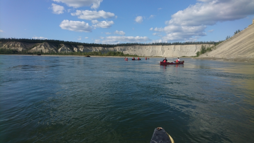 Canoe group exploring a scenic river with canyon walls.