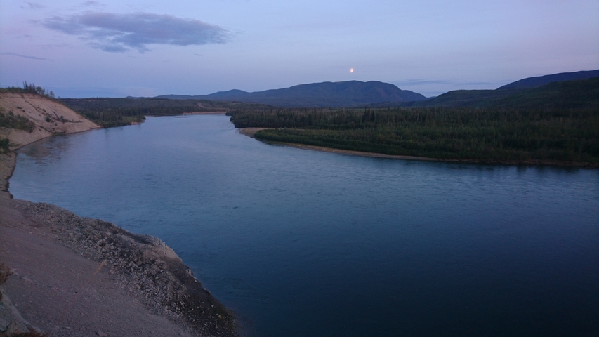 River landscape at dusk with a distant moon and mountains.