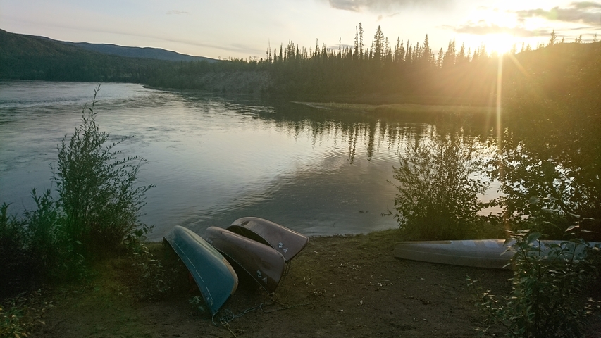 Canoes on the river bank at sunrise with warm light.