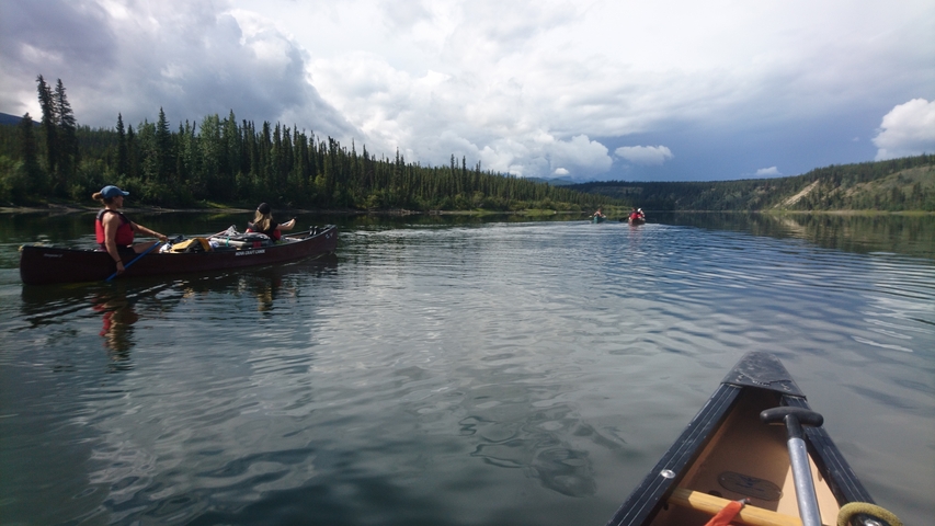 Group canoeing on a serene river with an approaching storm.