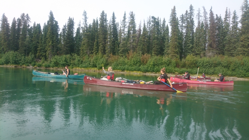 People canoeing on a calm river surrounded by trees.