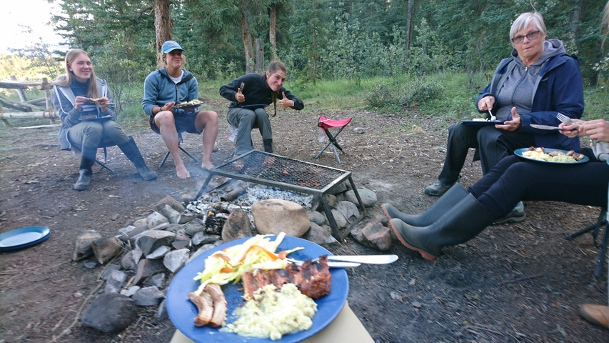Friends enjoying a meal around campfire.