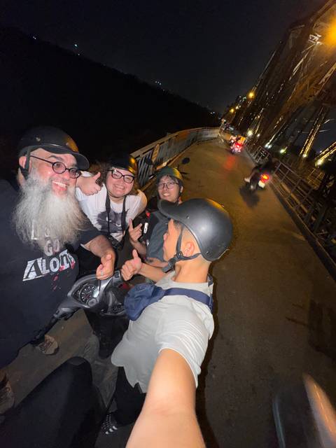 Group of people posing on scooters at night on a city street.