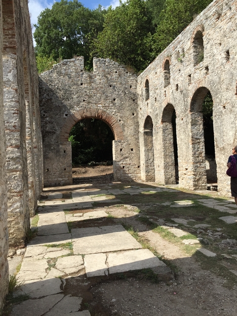 A person standing near ancient stone arches in a sunlit area.