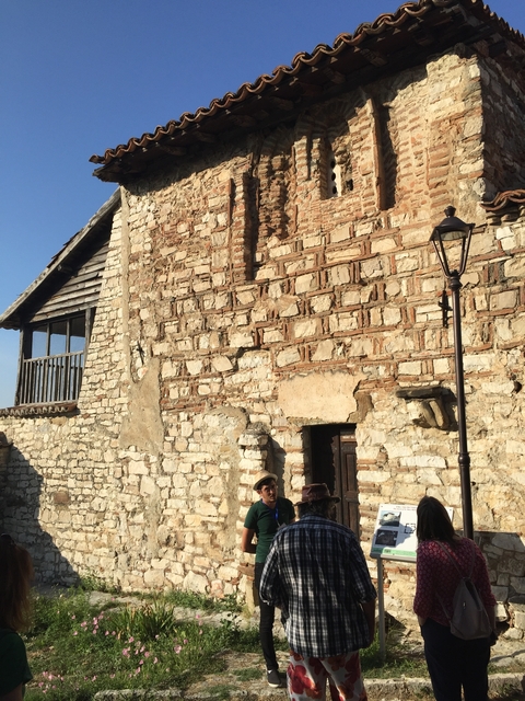 People walking by an old stone building with a window.