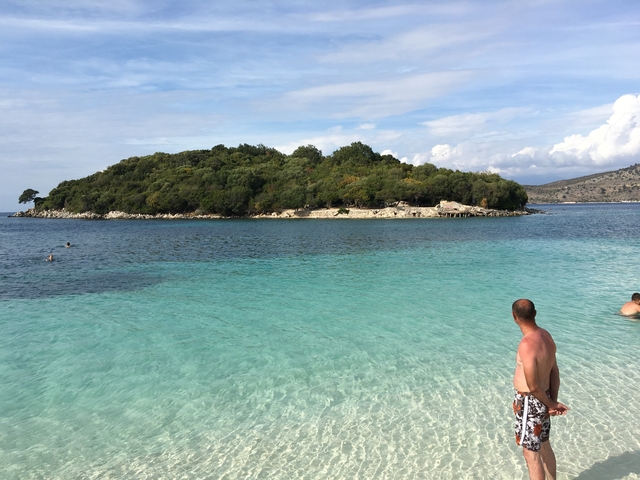 Person standing in a clear blue sea with an island view.