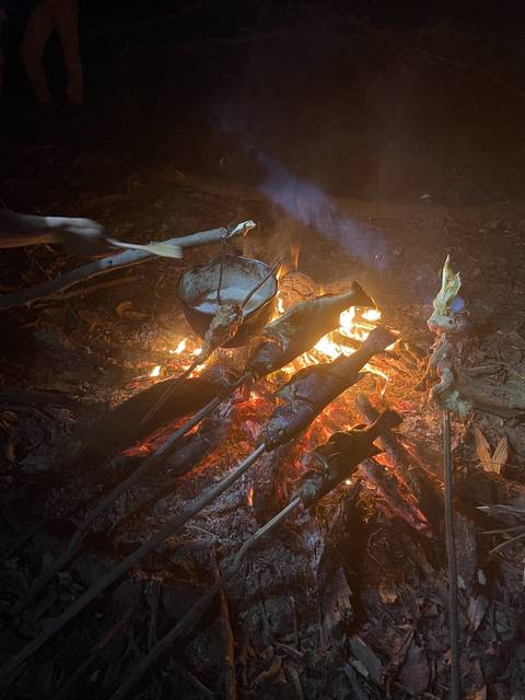 Campfire cooking with food skewered over flames.
