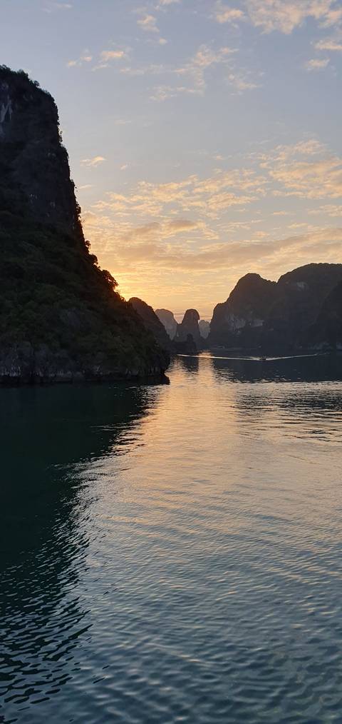 Sunset view of Halong Bay with silhouette of limestone islands.