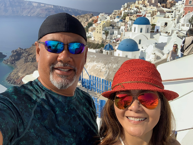 Couple smiling with the iconic blue domes of Santorini in the background.
