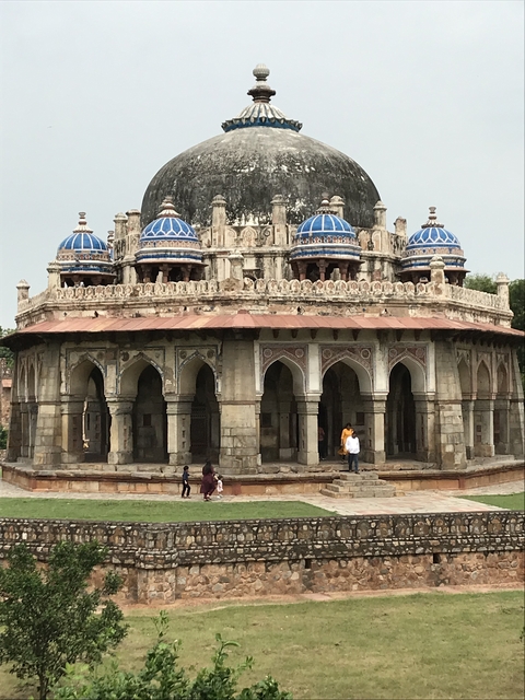 People walking around an ornate tomb structure with blue domes.