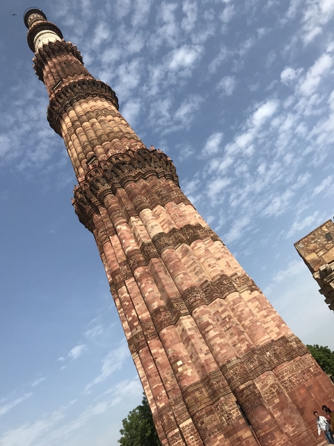 Tilted view of Qutub Minar, a historic red sandstone tower against blue skies.