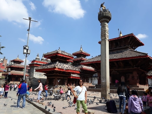 People in front of traditional temples with pigeons scattered around.