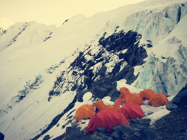 Tents on a snowy mountainside with jagged peaks.