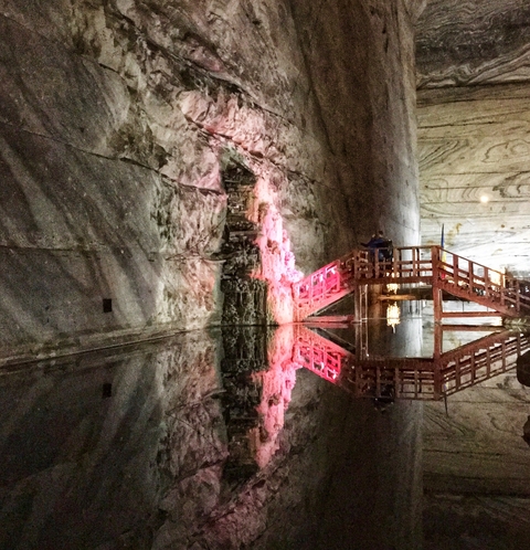 A cave with a reflective pool and wooden structure illuminated by pink light.