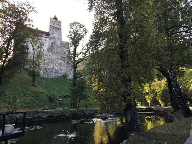 A castle with surrounding greenery and a water body in the foreground.