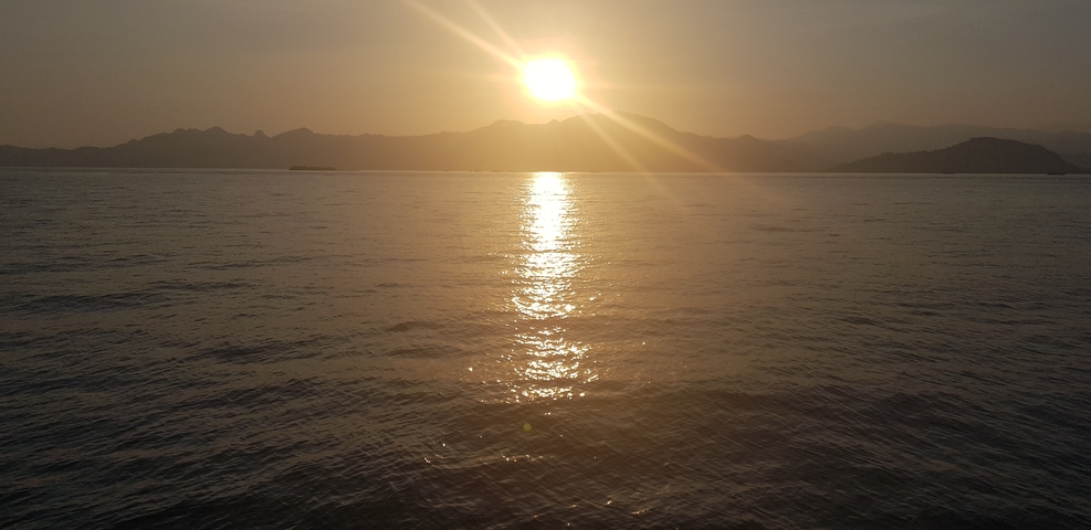 Sunset over a calm sea with silhouetted mountains.