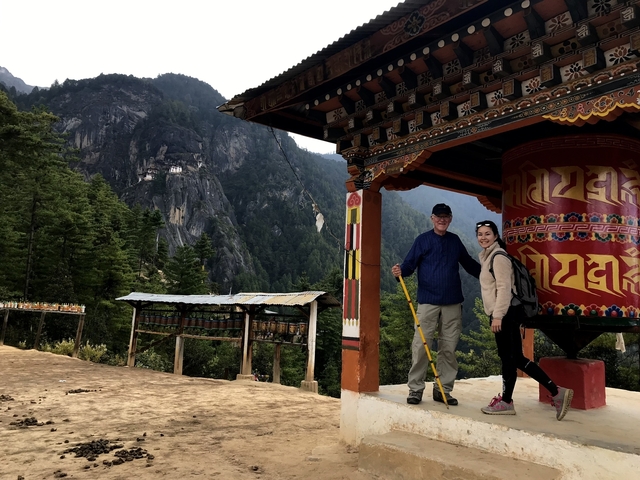 Couple at a prayer wheel with a mountain monastery in the background.