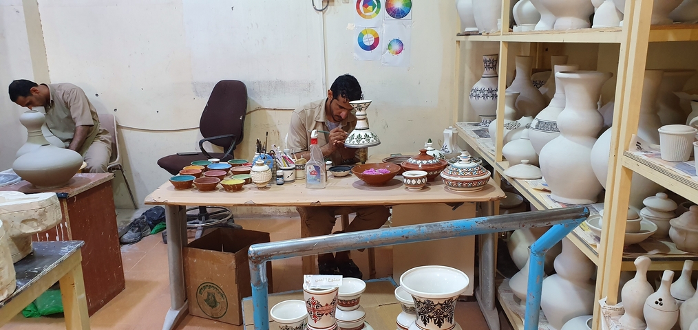 A man painting pottery inside a workshop.