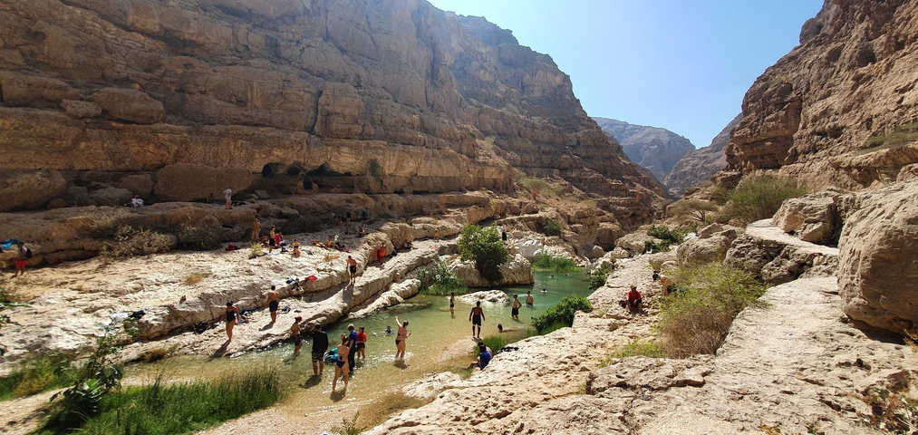 A crowded natural limestone canyon pool with people swimming.