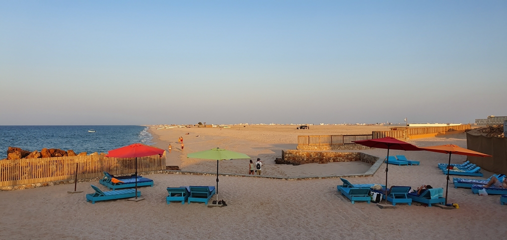 Beach with loungers and parasols, people enjoying the sandy coastline.