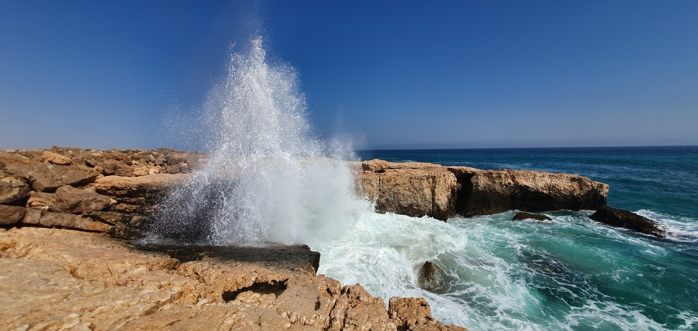 Ocean waves crashing against rocky cliffs with deep blue water.