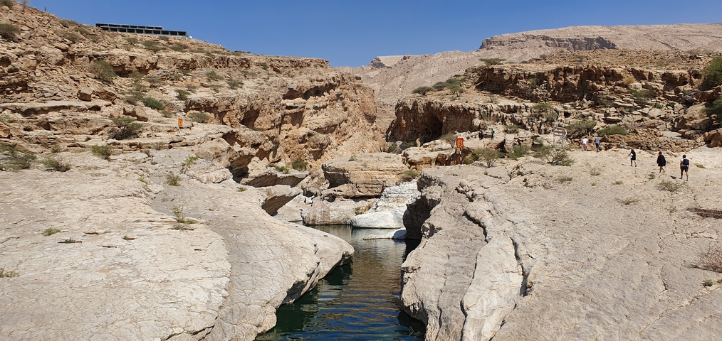A rugged canyon with a clear stream running through, people walking.