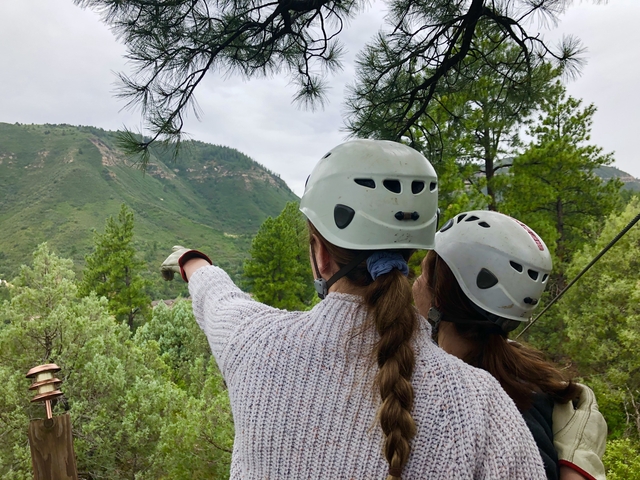 Two people with helmets pointing to a mountainous landscape.