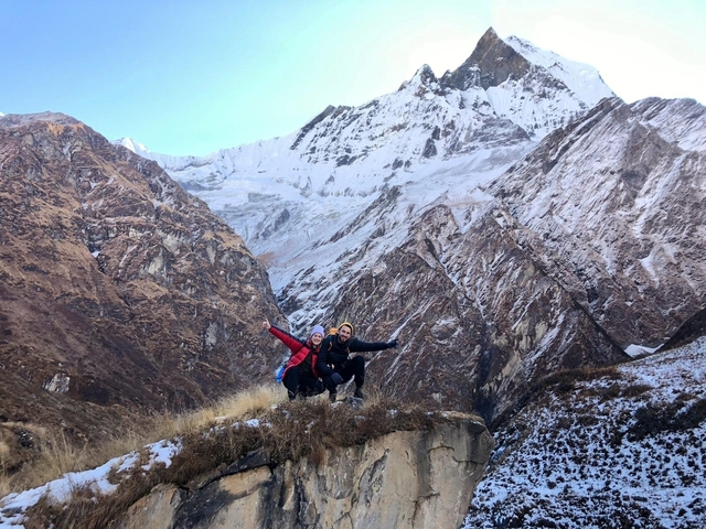 Two people posing with snow-covered mountains in the background