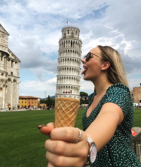 Woman playfully posing with the Leaning Tower of Pisa.