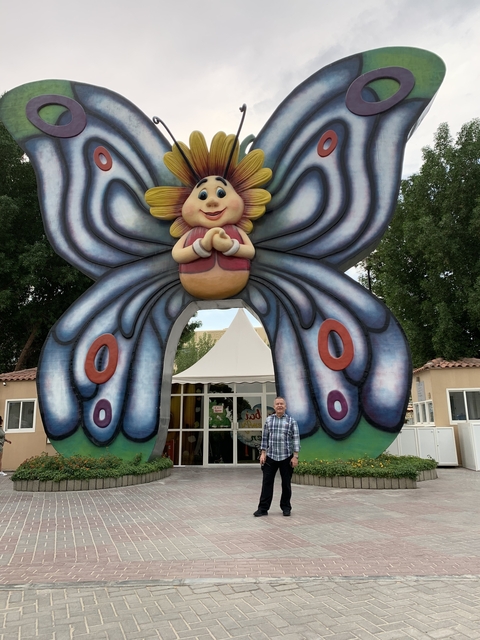 A man standing beneath a large butterfly sculpture outside.