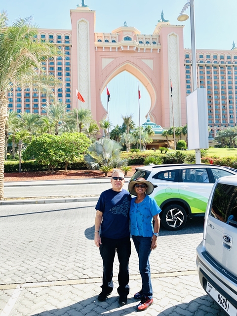 A couple standing in front of a large hotel entrance with palm trees.