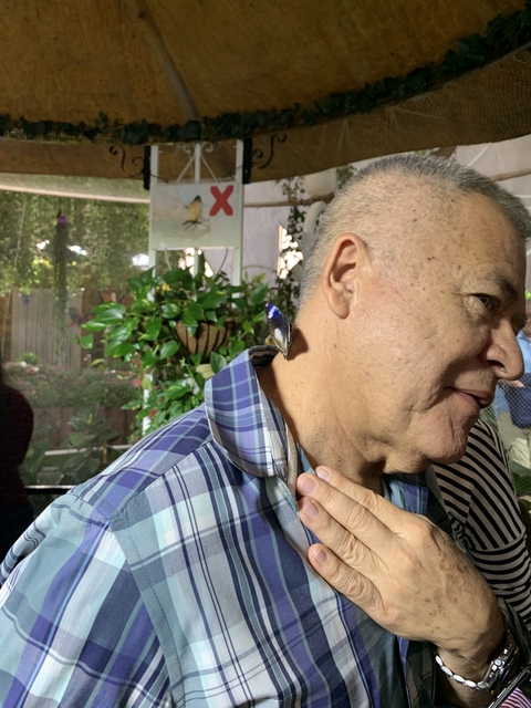 A close-up of a man with a butterfly perched on his shoulder.