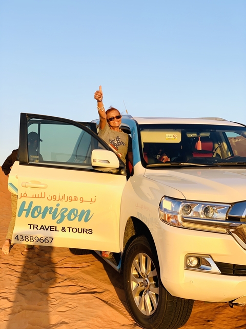 A woman standing with an arm out of a car door in the desert.