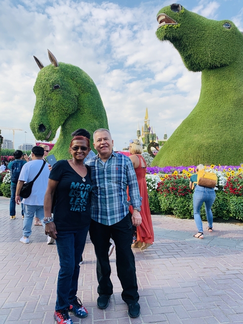 A couple posing in a garden with large green sculptures in the background.