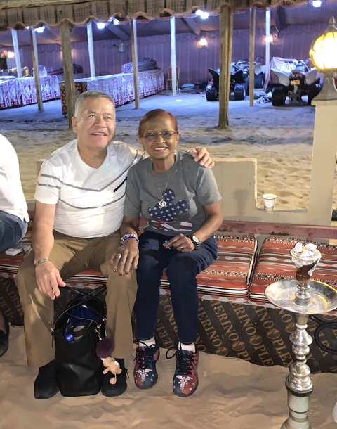 A couple seated on a carpet in a desert setting with a hookah.