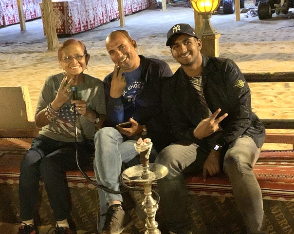 A woman and two men posing with a hookah on a desert carpet.