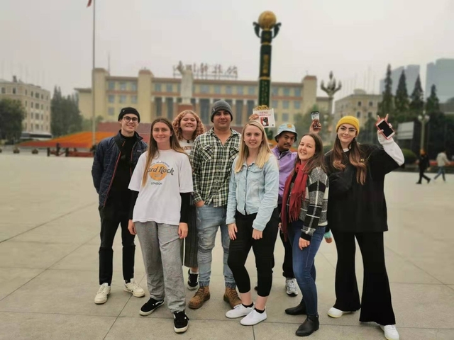 Group of travellers posing in a city square with a government building in hazy conditions.