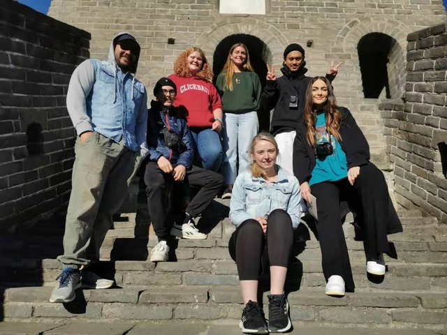 Smiling tour group sitting on stone steps along the Great Wall of China on a sunny day.