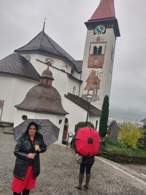 Person holding an umbrella near a church with murals.