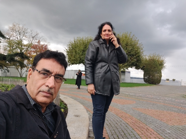 Couple posing in a park setting with trees and overcast sky.