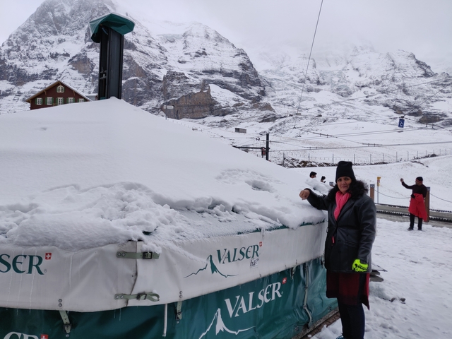 Person next to a snow-covered structure with mountains in the background.