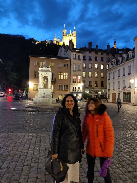 Two people posing in a cobblestone square, well-lit at night.