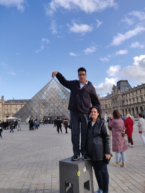 Two people posing in front of the Louvre Pyramid.