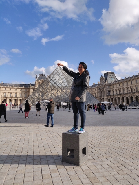 Woman interacting with the Louvre Pyramid in an optical illusion photo.