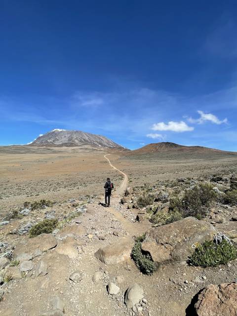 Hiker walking on a mountainous trail with clear sky.