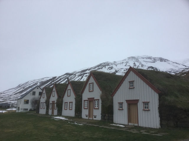 A house with snowy mountains in the background near a body of water.