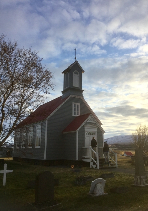 A small church with a red roof set against a cloudy sky.