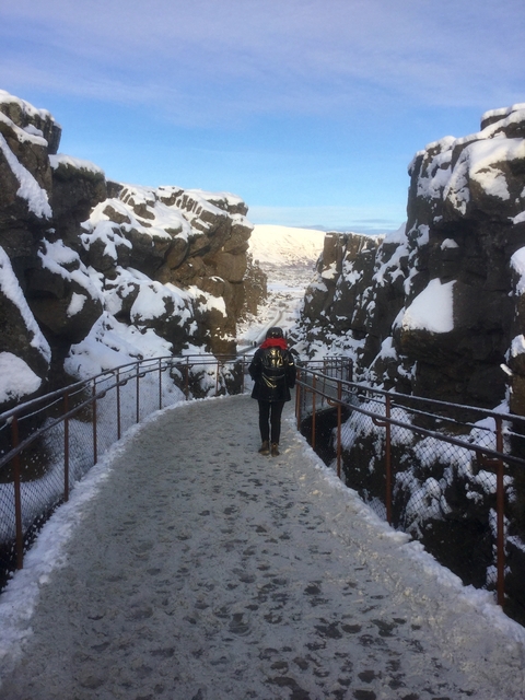 A person walking on a snowy path between rock formations.