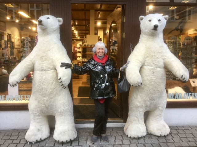 A person posing with two large polar bear statues outside a shop.