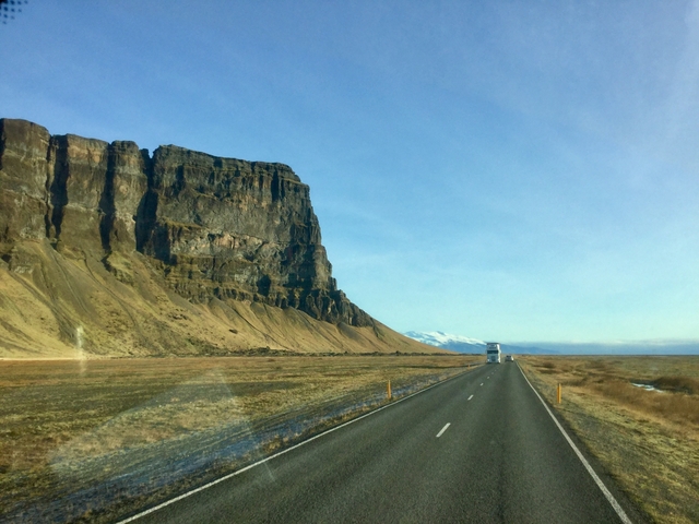 A long road leading to a distant mountain under a clear blue sky.